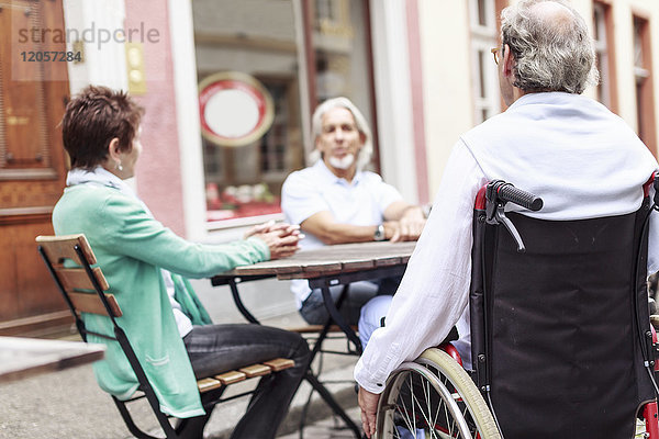 Deutschland  Heidelberg  Senior im Rollstuhl mit Freunden in einem Straßencafé