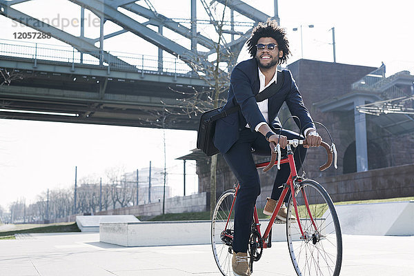 Lächelnder Geschäftsmann beim Fahrradfahren an der Flussbrücke