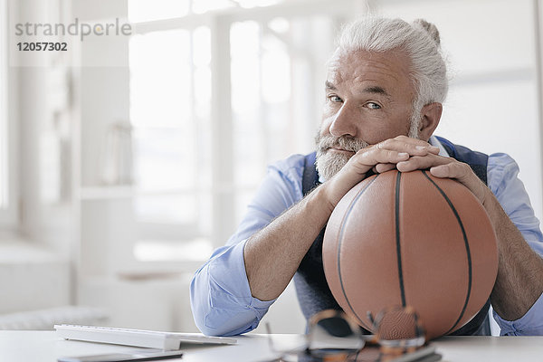Porträt eines reifen Mannes am Schreibtisch mit Basketball