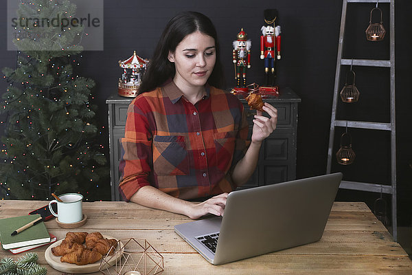 Junge Frau mit Laptop beim Croissantessen zur Weihnachtszeit