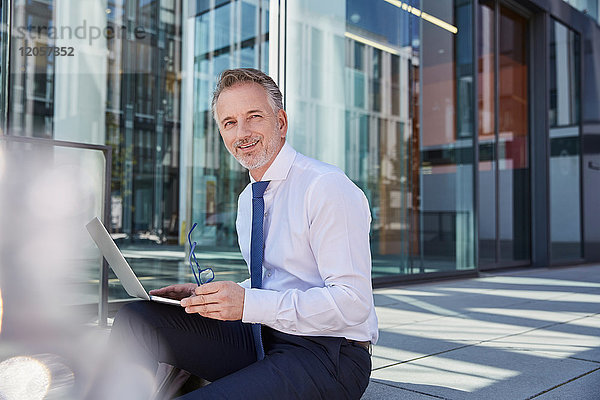 Portrait eines lächelnden Geschäftsmannes mit Laptop im Freien