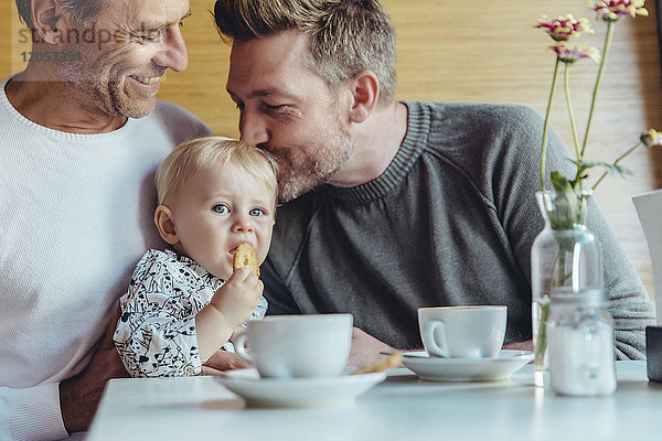 Schwules Paar kuschelt mit seinem Baby im Cafe