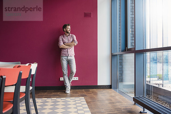 Mann lehnt sich an lila Wand im modernen Büro und schaut aus dem Fenster.