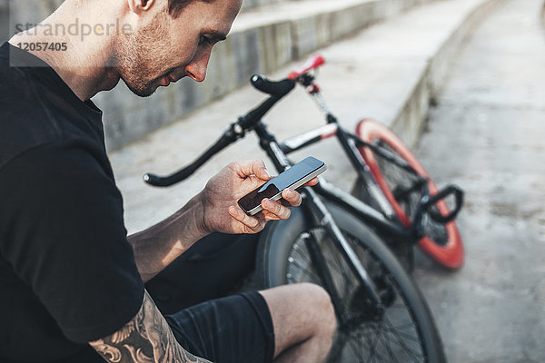 Junger Mann sitzt neben fixie bike mit Handy