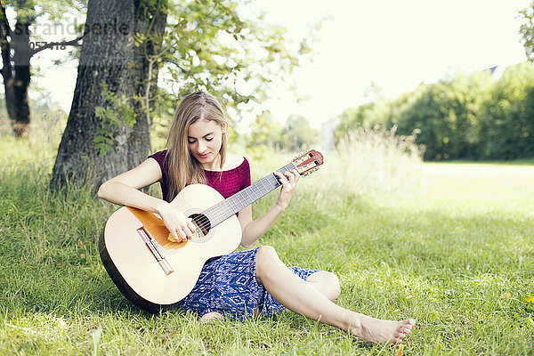Junge Frau auf der Wiese sitzend  Gitarre spielend