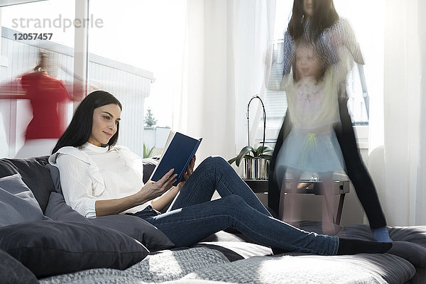Mädchen springen auf dem Sofa  während die Mutter ein Buch liest.