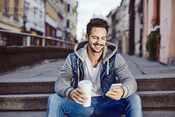 Mann mit Kaffee sitzt auf der Treppe in der Stadt mit dem Telefon