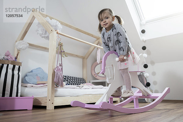 Kleinkind Mädchen rockt auf Schaukelpferd im Kinderzimmer