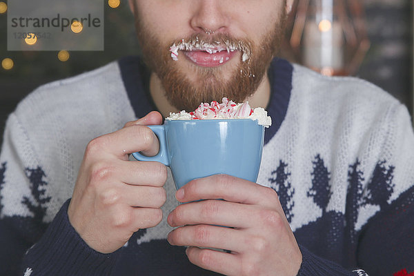 Mann trinkt heiße Schokolade mit Schlagsahne und gehackten Zuckerstangen zur Weihnachtszeit