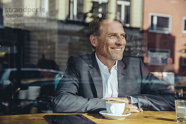 Lächelnder Geschäftsmann im Café mit Blick aus dem Fenster