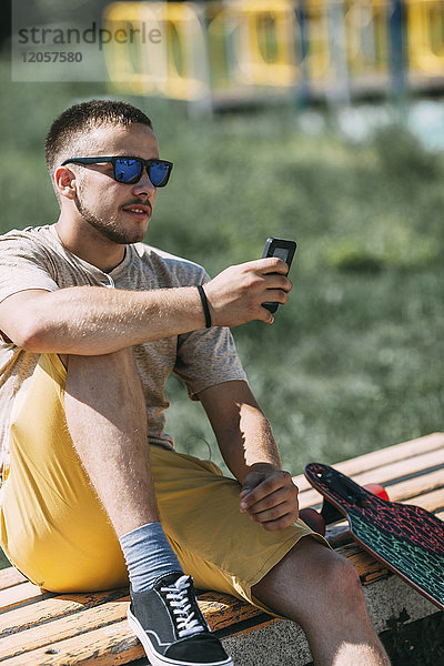 Junger Mann sitzend auf einer Bank mit Handy