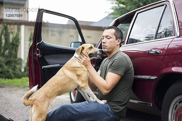 Mann sitzt neben dem Auto und spielt mit dem Hund