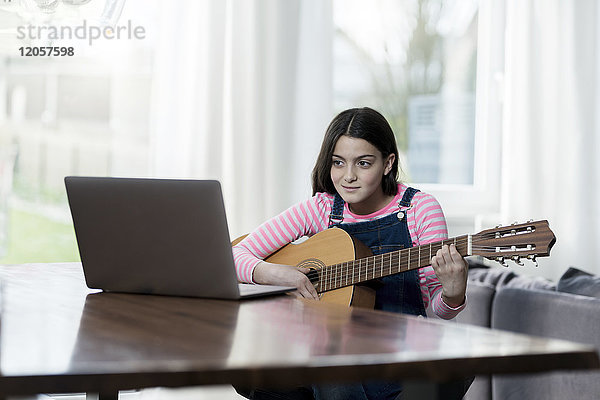 Mädchen spielt Gitarre vor dem Laptop
