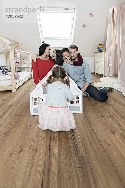 Glückliche Familie mit drei Töchtern beim Spielen mit Puppenhaus im Kinderzimmer