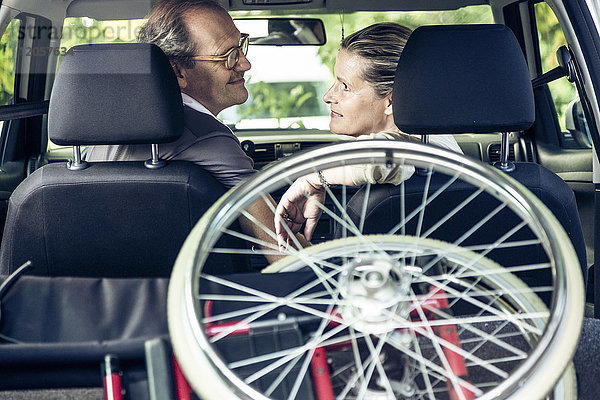Lächelndes Paar im Auto mit Rollstuhl im Kofferraum