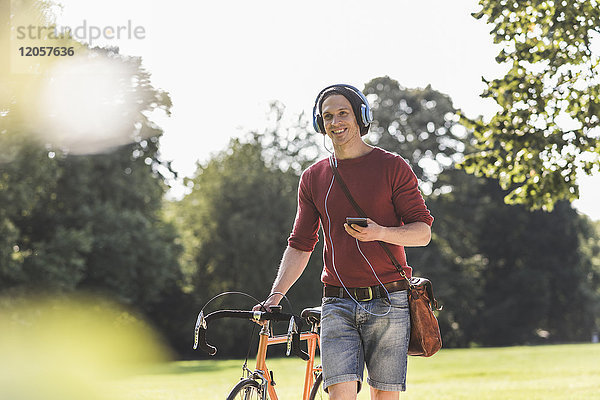 Lächelnder Mann mit Rennrad Musik hören mit Kopfhörern im Park