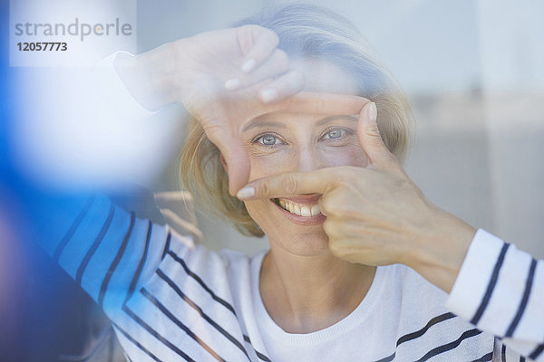 Porträt einer lachenden blonden Frau  die mit ihren Fingern einen Rahmen baut  während sie den Betrachter ansieht