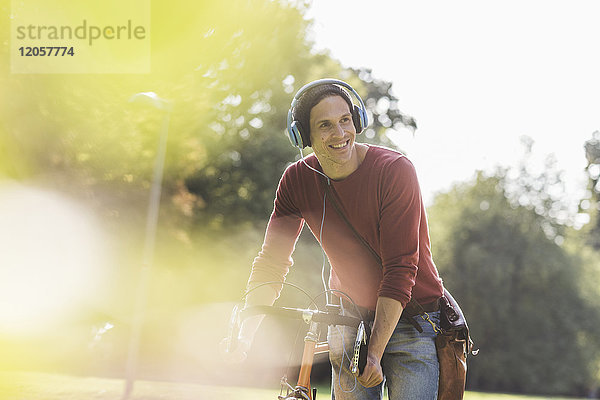 Porträt eines lächelnden Mannes mit Rennrad  Musik hören mit Kopfhörern im Park