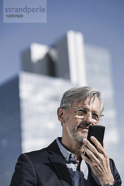 Grauhaariger Geschäftsmann spricht ins Smartphone