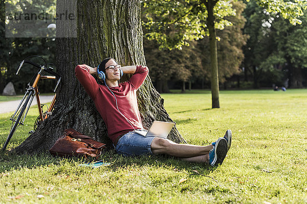 Mann mit Laptop und Kopfhörer entspannt im Park