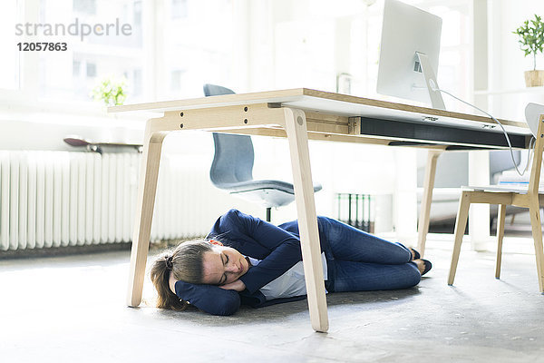 Geschäftsfrau unter dem Tisch liegend im Büro schlafend