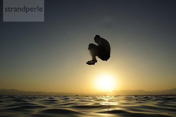 Mann  der bei Sonnenuntergang ins Meer springt.