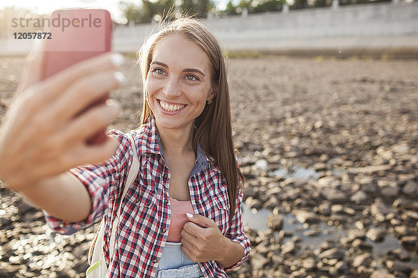Porträt einer glücklichen jungen Frau auf dem Handy am Flussufer