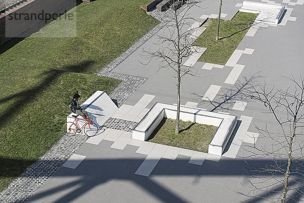 Mann sitzt im Stadtskatepark mit Smartphone neben seinem Fahrrad