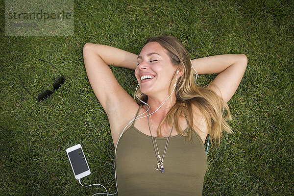 Fröhliche junge Frau mit Kopfhörern auf dem Rasen