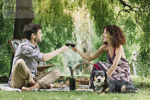 Pärchen mit Hund beim Picknick im Park beim Rotweintrinken