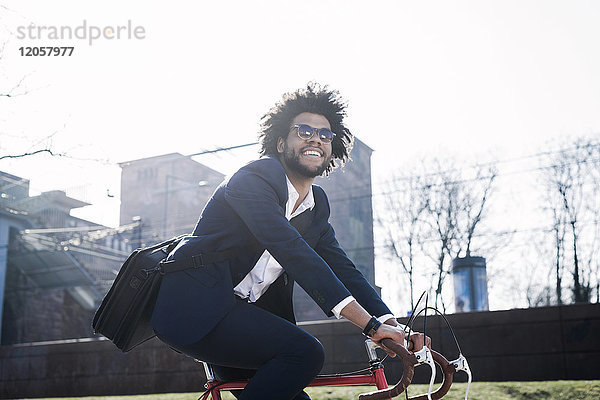 Lächelnder Geschäftsmann mit Sonnenbrille auf dem Fahrrad in der Stadt