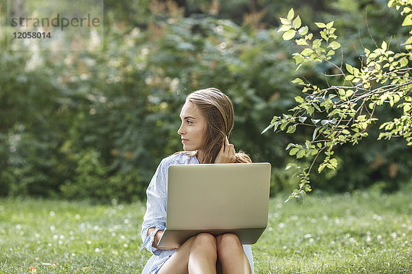 Junge Frau mit Laptop auf einer Wiese mit Blick zur Seite