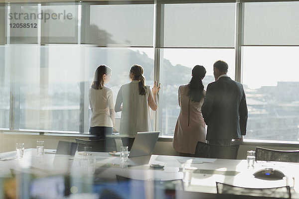 Geschäftsleute schauen aus einem sonnigen Fenster in einem städtischen Konferenzraum
