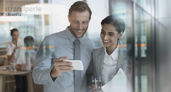 Lächelnder Geschäftsmann und Geschäftsfrau  die ein Video auf einem Smartphone im Büro ansehen