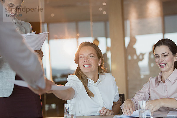 Lächelnde Geschäftsfrau  die einem Kollegen in einem Konferenzraum Papierkram übergibt