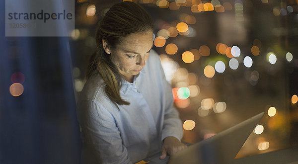 Seriöse  konzentrierte Geschäftsfrau  die nachts am Laptop im Bürofenster arbeitet
