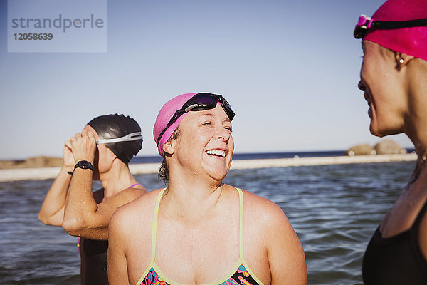 Lachende Schwimmerinnen sprechen am sonnigen Ozean