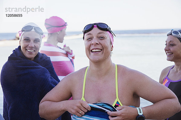 Portrait lächelnde  selbstbewusste Schwimmerinnen  die mit Handtüchern abtrocknen.