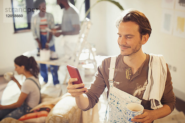 Mann malt Wohnzimmer  trinkt Kaffee und überprüft Smartphone