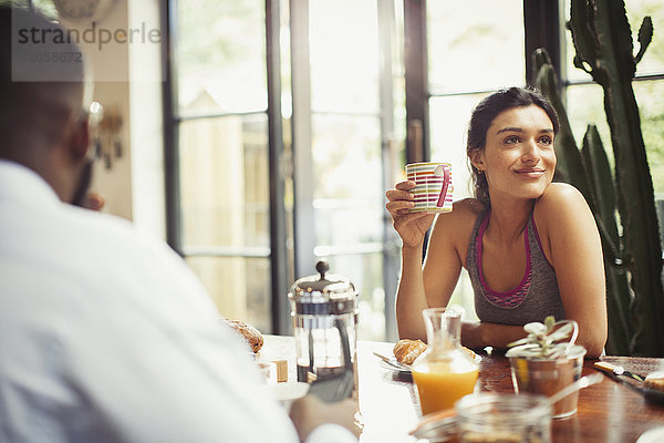 Lächelnde Frau beim Kaffeetrinken am Frühstückstisch