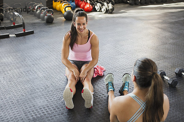 Junge Frauen beim Sprechen und Strecken der Beine im Fitnessstudio