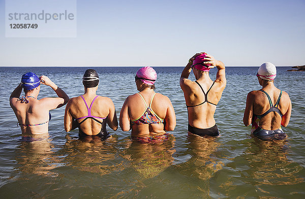 Weibliche Schwimmerinnen stehen in einer Reihe in sonniger Meeresbrandung.