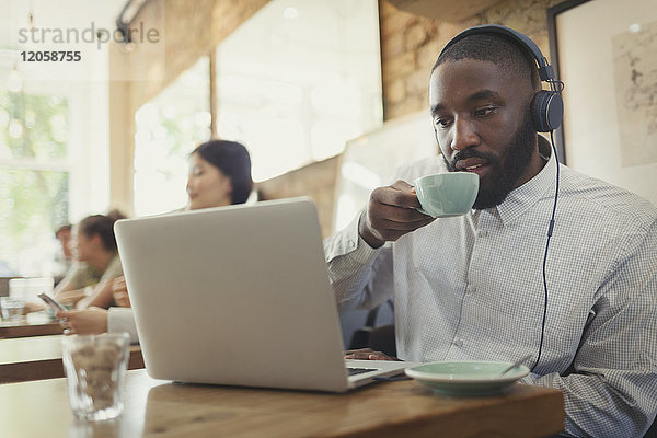 Mann mit Kopfhörer mit Laptop und Kaffeetrinken im Cafe