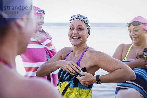 Lächelnde Schwimmerinnen  die mit Handtüchern am Strand trocknen