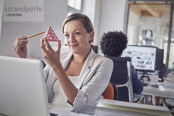 Lächelndes weibliches Design-Profi untersucht Dreieck-Prototyp am Laptop im Büro