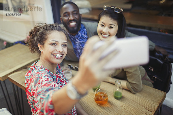 Lächelnde junge Freunde nehmen Selfie mit Fotohandy am Bürgersteig Cafe