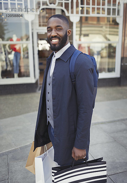 Portrait lächelnder  selbstbewusster junger Mann mit Einkaufstaschen vor der Fassade