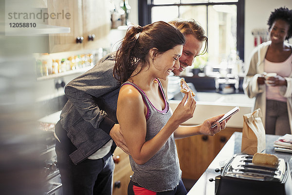 Lächelndes Paar SMS mit Smartphone  Toast essen in der Küche