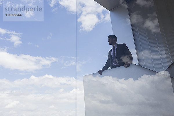 Geschäftsmann auf modernem Balkon mit Blick aus dem Fenster auf blauen Himmel und Wolken