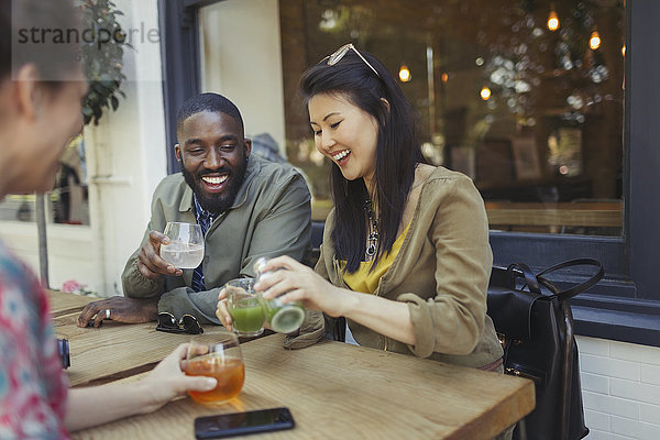 Lächelnde junge Freunde trinken Saft im Straßencafé